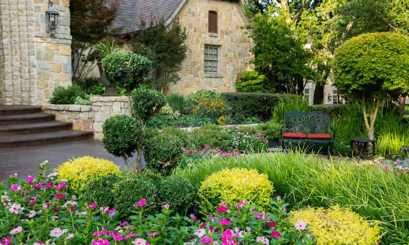 landscaped home entrance with plants flowers shrubs bushes trees and seating bench